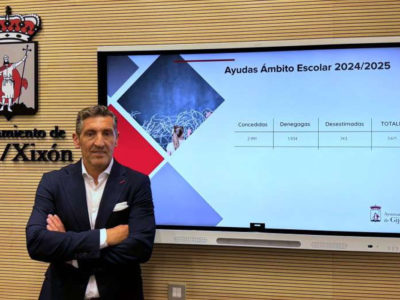 Conceyal d’Educación del Conceyu de Xixón delantre d’una pantalla con información sobre ayudes escolares.