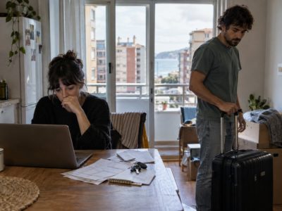 Dos persones nun pisu, una d’elles énte un ordenador y otra preparando una maleta, nuna imaxe sobre inestabilidá residencial.