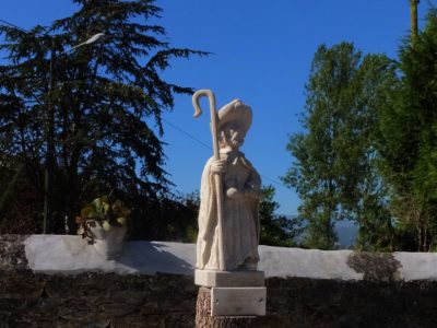 Escultura de Santiago Apóstol sobre un troncu, con árboles y cielu azul al fondu, en La Manxoya.