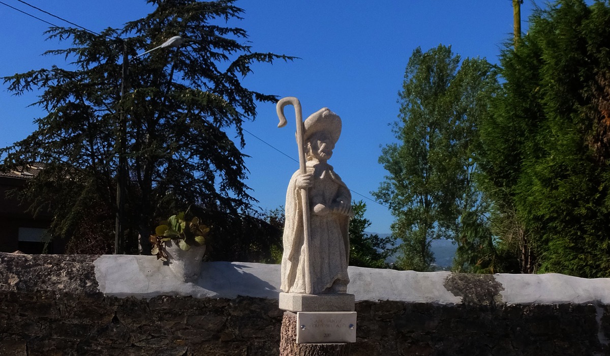 Escultura de Santiago Apóstol sobre un troncu, con árboles y cielu azul al fondu, en La Manxoya.