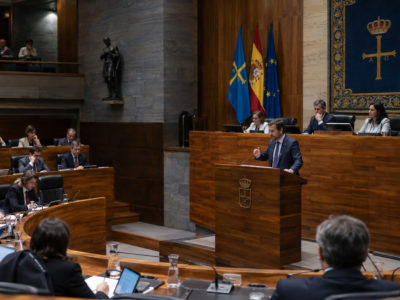 Vista d’una sesión parlamentaria recreada con persones sentaes en bancos y una intervención dende una tribuna